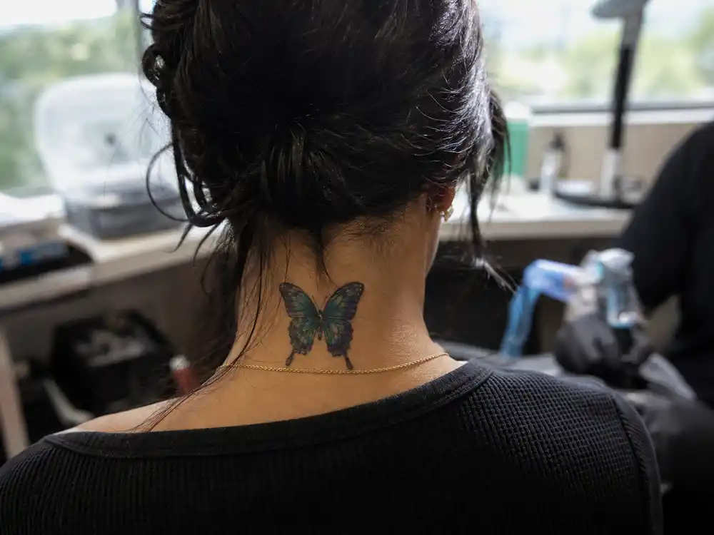 Vanessa Hudgens tattoos and their meanings — close-up of colorful butterfly neck tattoo on back of neck from over-shoulder angle