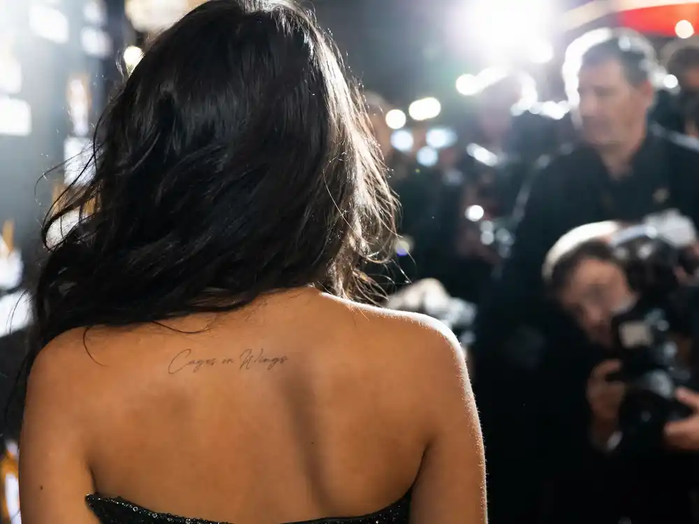 Vanessa Hudgens tattoos and their meanings — Cages or Wings script tattoo on left shoulder from over-shoulder premiere angle