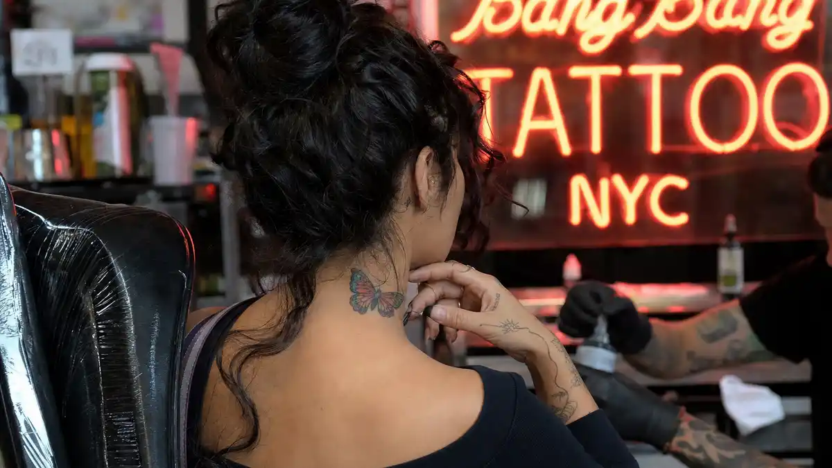 Vanessa Hudgens tattoos and their meanings — actress seen from behind in Bang Bang Tattoo studio with colorful butterfly neck tattoo and fine-line hand ink visible