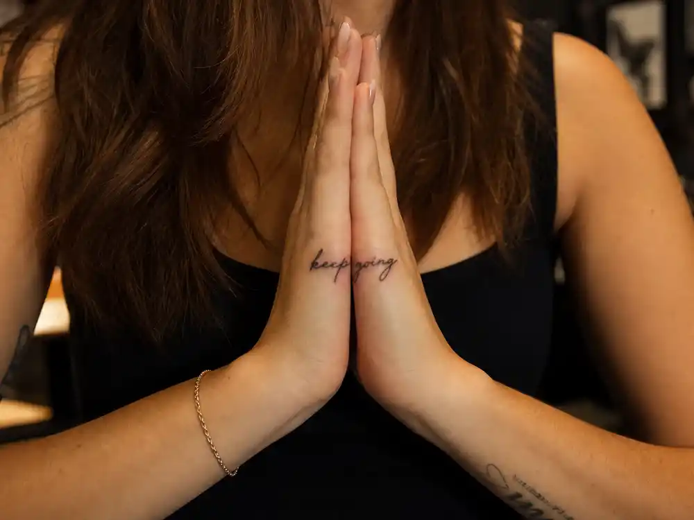 Vanessa Hudgens tattoos and their meanings — split Om symbol tattoos on pinky fingers forming complete symbol when hands pressed together