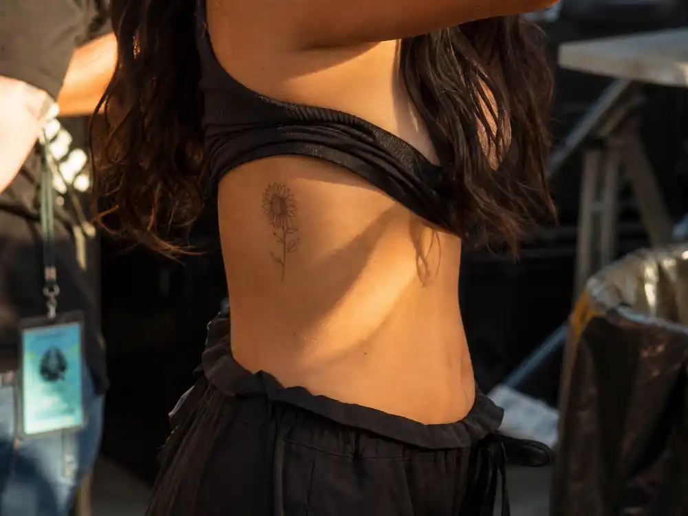 Vanessa Hudgens tattoos and their meanings — tiny fine-line sunflower tattoo on side rib photographed from side angle
