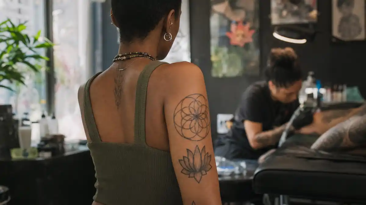 Willow Smith tattoos and their meanings — musician seen from behind in tattoo studio with spiritual arm ink and lotus tattoos visible