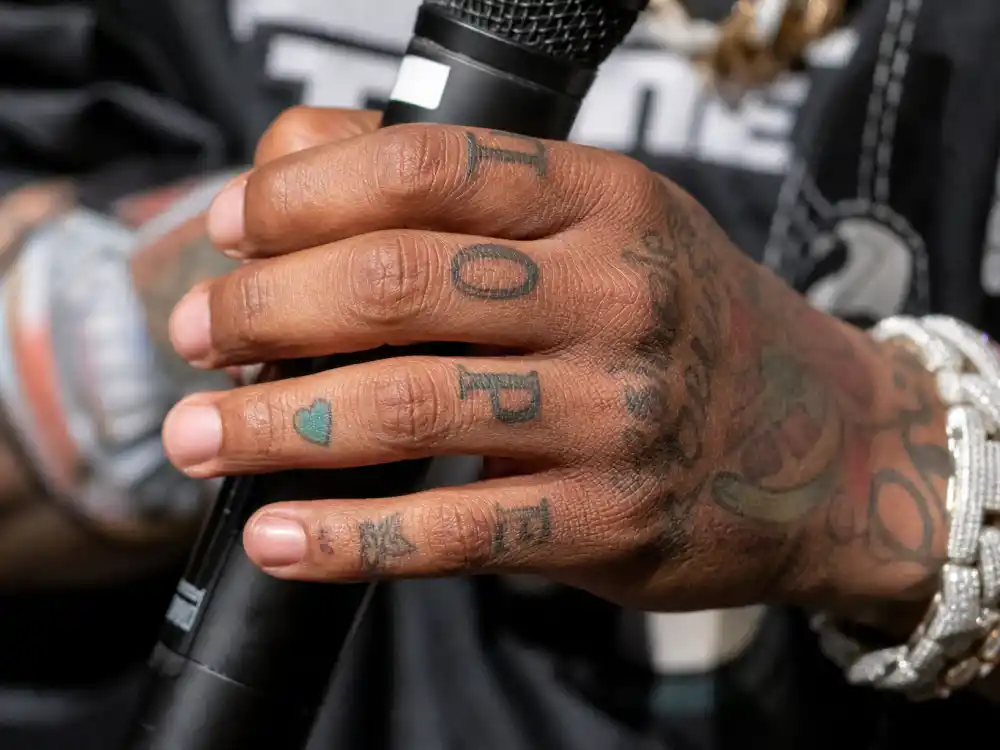 Wiz Khalifa tattoos and their meanings — tattooed fingers and knuckles with letter ink on rapper hands holding microphone backstage