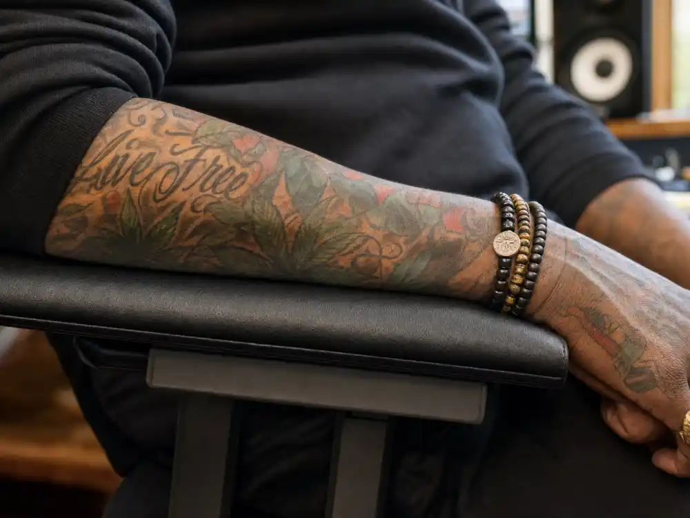 Wiz Khalifa tattoos and their meanings — close-up of colorful forearm sleeve with cannabis leaf and script motifs on rapper arm