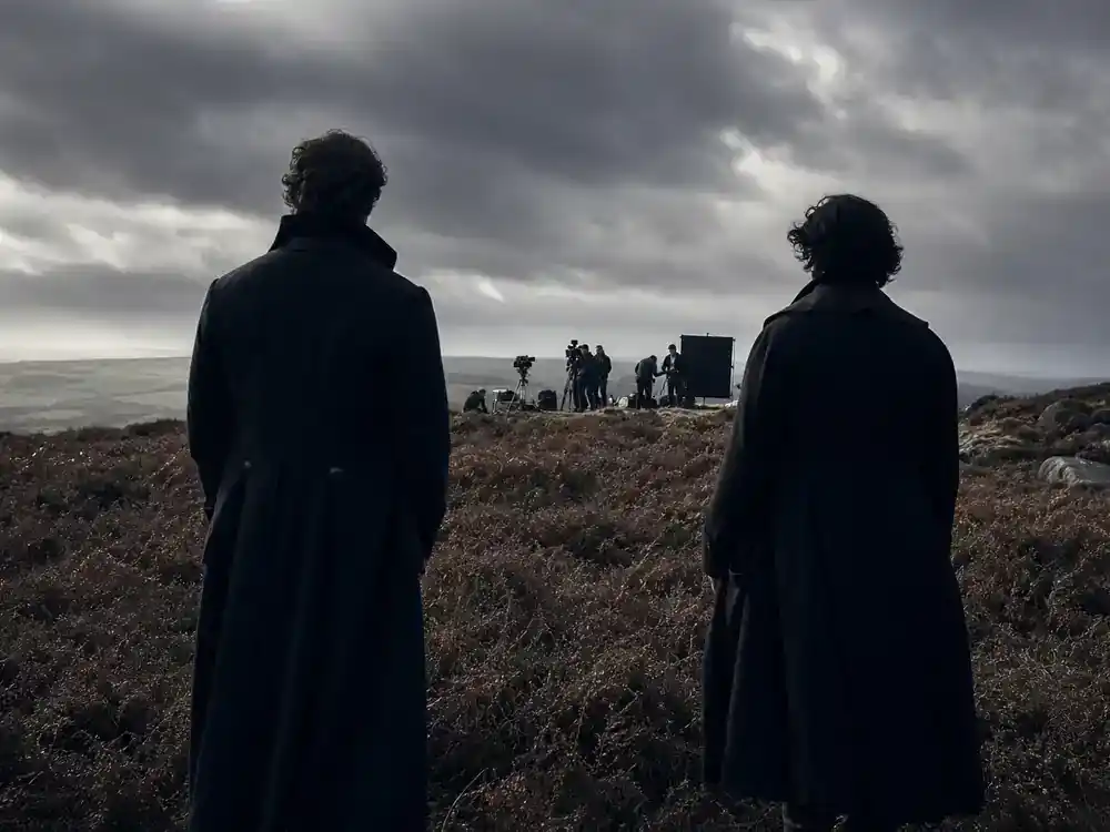 Wuthering Heights Margot Robbie movie cast guide Heathcliff — two actor silhouettes rehearsing on windswept moor film location from behind, stormy sky