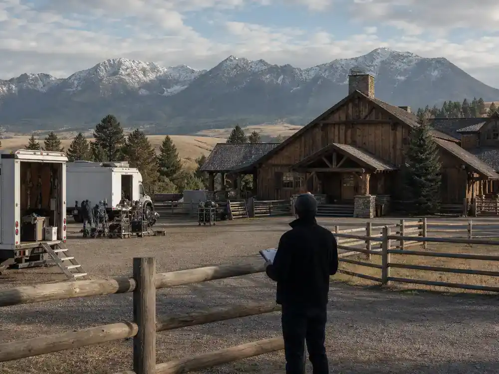 Yellowstone filming locations Montana guide Chief Joseph Ranch — historic Montana ranch lodge exterior with film trucks on gravel drive and mountain backdrop