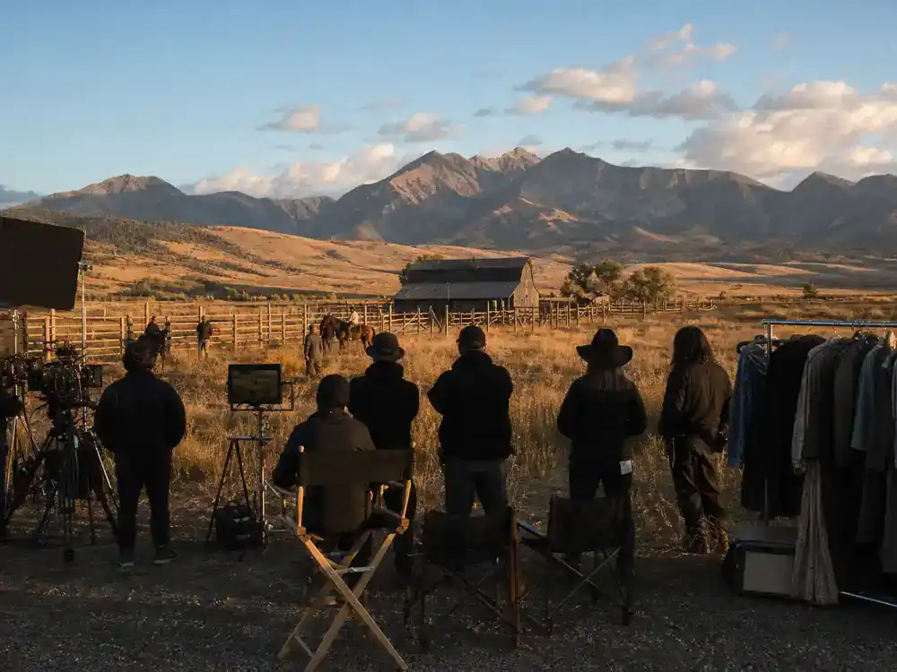 Yellowstone filming locations Montana guide Montana ranch — TV western drama production set with director chairs wardrobe racks and crew silhouettes on valley ranch land