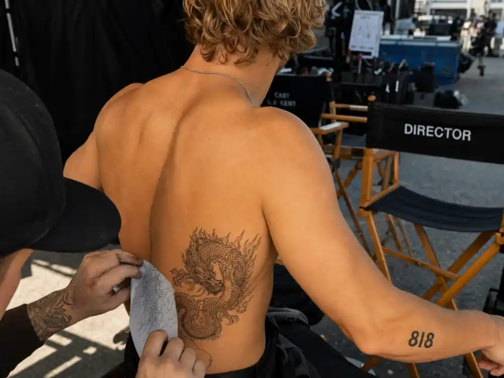 Zac Efron tattoos and their meanings — temporary dragon rib tattoo and 818 forearm numbers applied on We Are Your Friends movie set