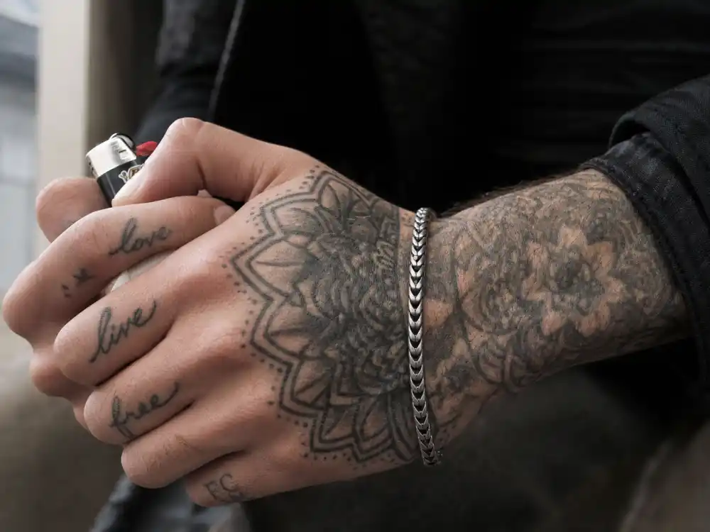 Zayn Malik tattoos and their meanings hand tattoos — finger script and knuckle ink close-up holding lighter