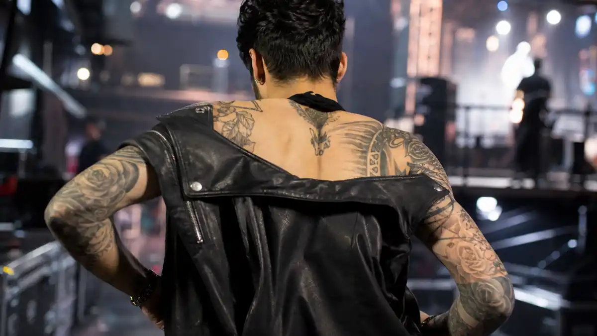 Zayn Malik tattoos and their meanings — young man with dark styled hair from behind backstage showing rose and script arm sleeve tattoos