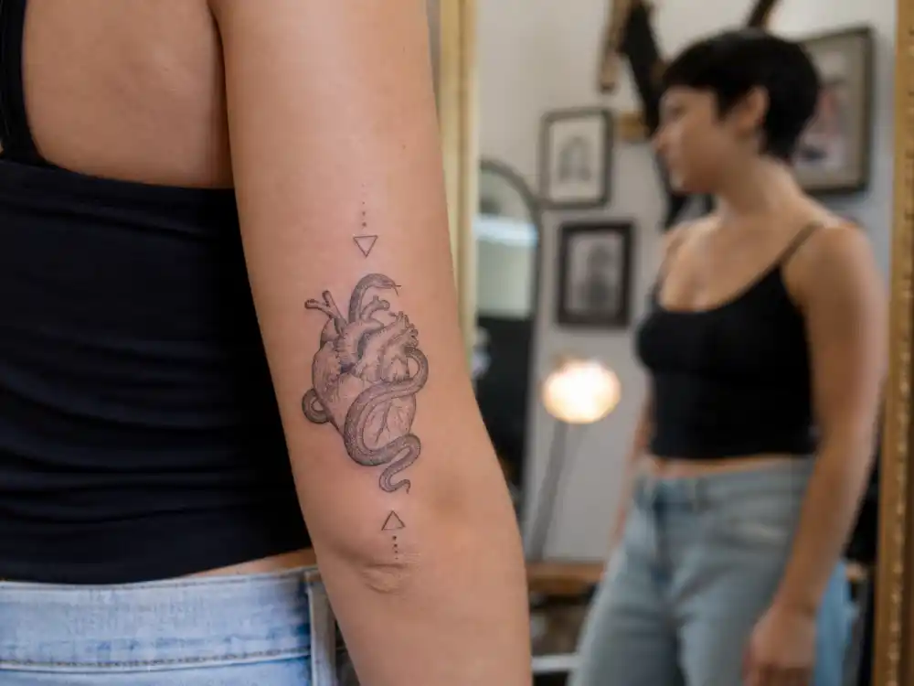 Zoe Kravitz tattoos and their meanings — snake wrapped around heart forearm tattoo plus geometric fine-line pieces in studio mirror