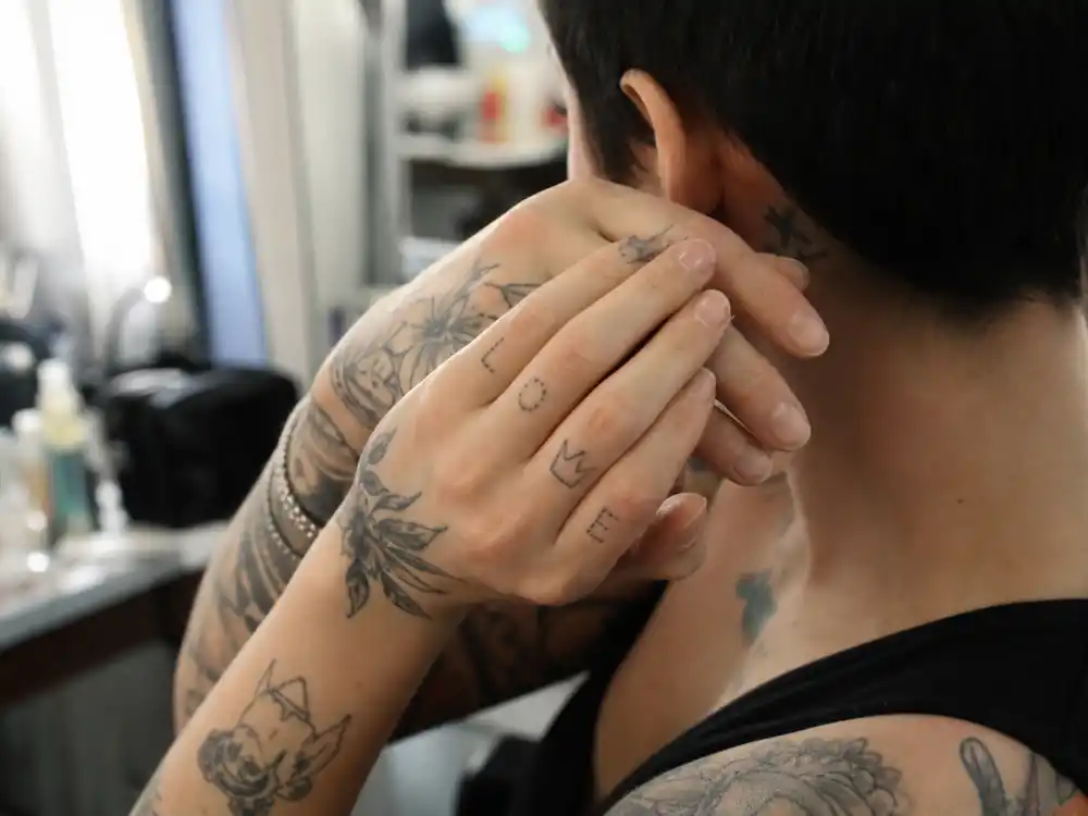 Zoe Kravitz tattoos and their meanings — close-up of Lola Wolf dotted finger script, leaf hand tattoos, and crown middle-finger ink
