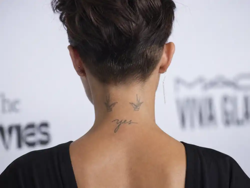 Zoe Kravitz tattoos and their meanings — swallow birds and yes script on back of neck photographed from behind at event