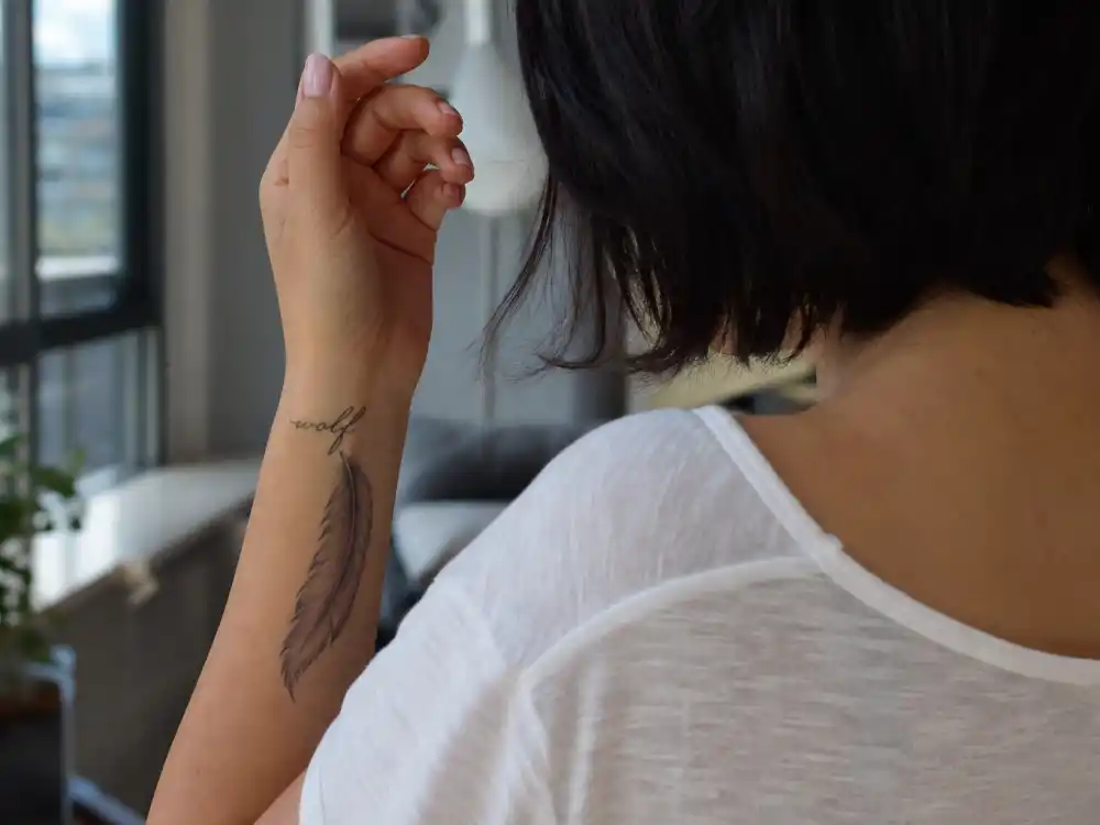 Zoe Kravitz tattoos and their meanings — wolf cursive wrist script and shaded feather tattoo on left wrist