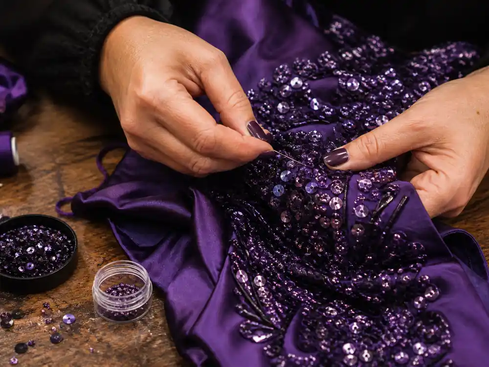 Hands stitching sequins on tour costume fabric tied to Beyonce net worth 2026