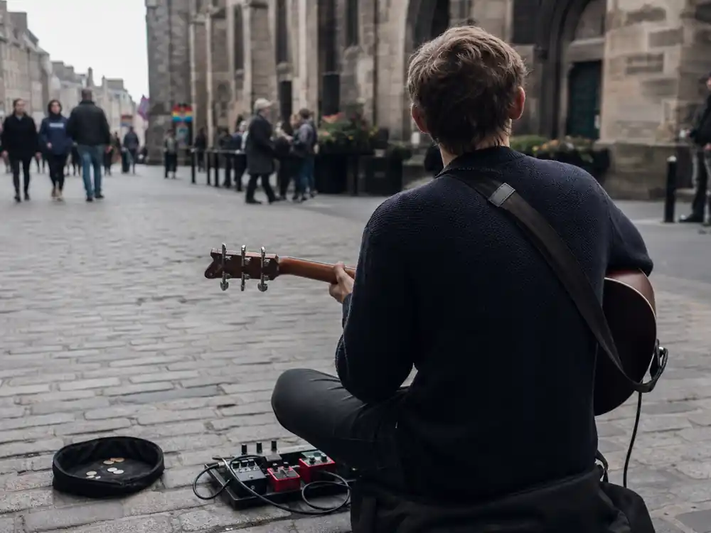 Street busker with loop pedal seen from behind tied to Ed Sheeran net worth 2026 humble start