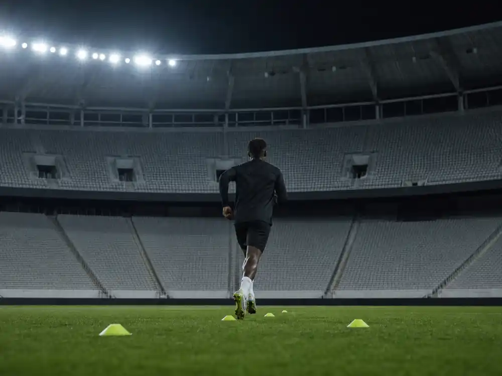Athlete silhouette training on an unmarked floodlit pitch at night, peak pay year in highest paid celebrities 2026