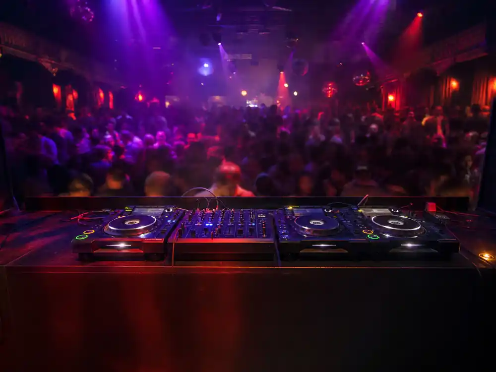 Nightclub DJ booth overlooking blurred crowd for how much is Drake worth streaming-era scale
